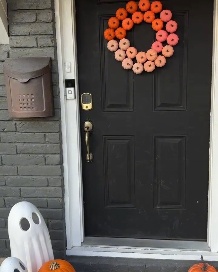 Ombre pumpkin wreath with orange, pink, and cream pumpkins on a black front door