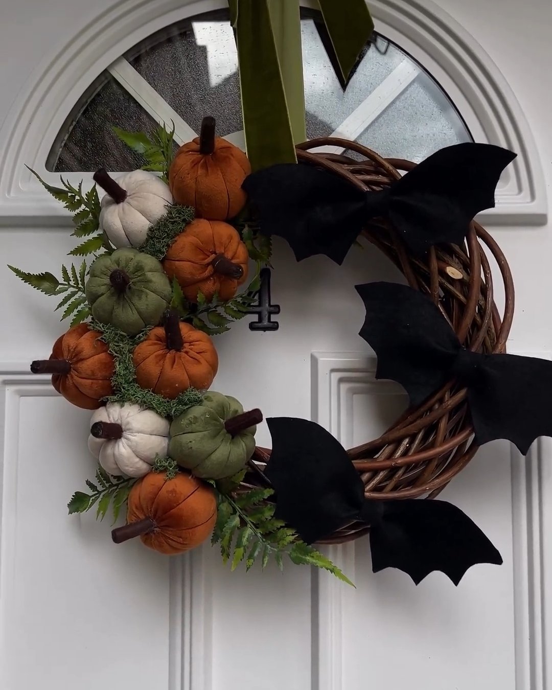 Orange, cream, and sage pumpkins with black bats on a grapevine Halloween door wreath