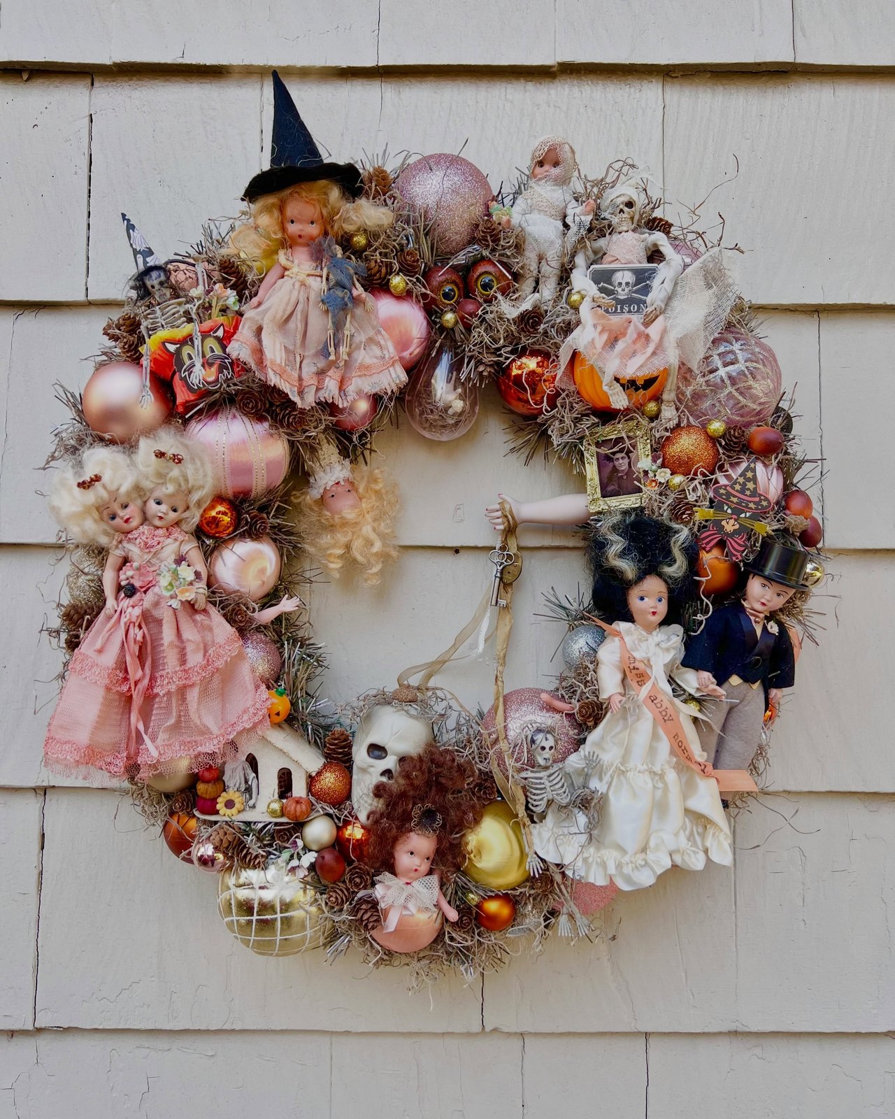 Vintage doll and skeleton Halloween door wreath with pumpkins, pinecones, ornaments, and moss