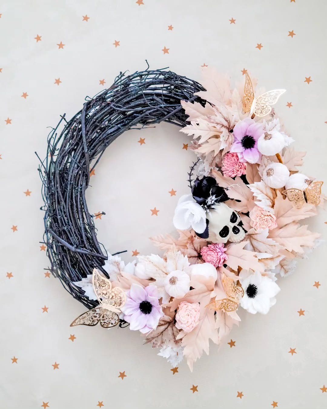 Black twig diy halloween wreath with blush flowers, pale leaves, butterflies, and a whimsical skull accent