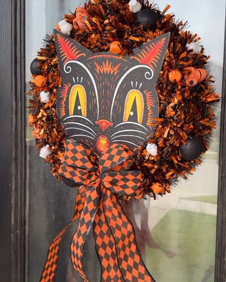 Orange and black cat face wreath with pumpkins, tinsel, ornaments, and harlequin bow for Halloween decor