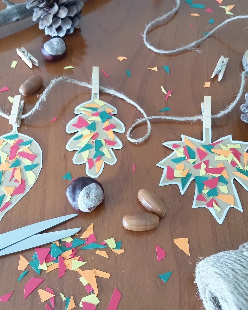 Colorful paper leaves clipped to twine with autumn craft materials and acorns