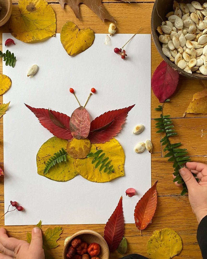 Leaf butterfly made from colorful autumn leaves, berries, and fern sprigs on white paper