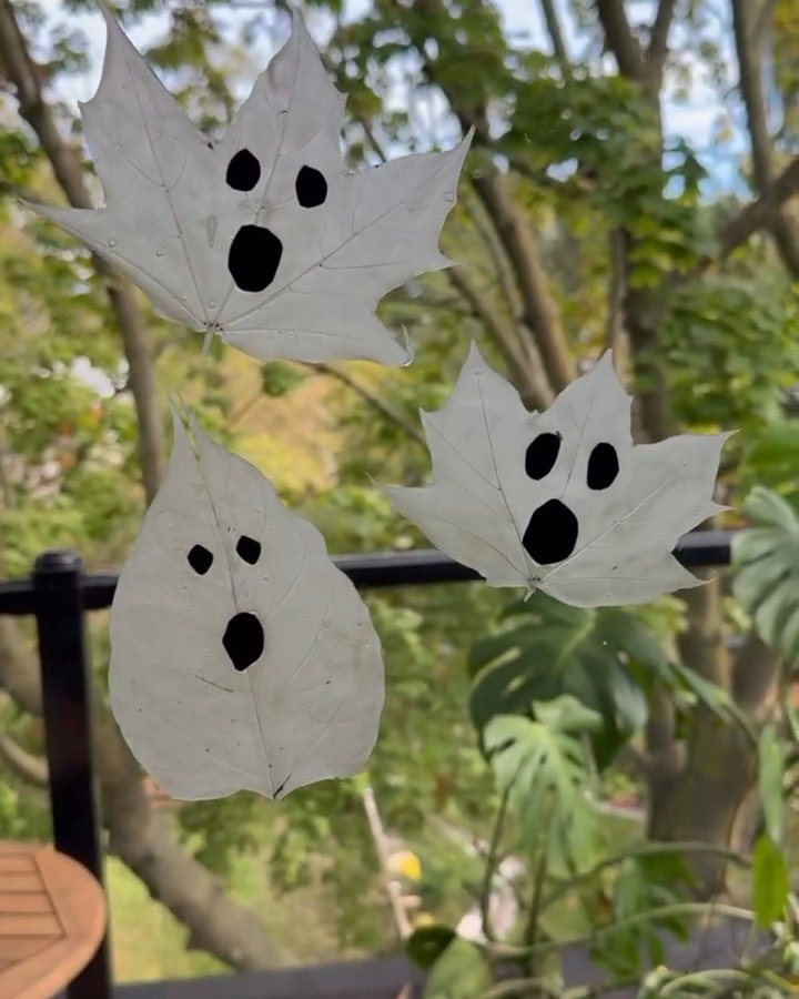 White leaf ghosts with black faces hanging outdoors among autumn greenery