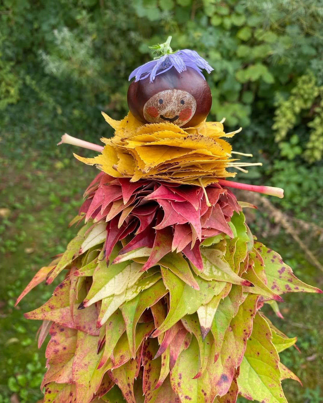 Conker fairy perched on layered red, yellow, and green autumn leaves outdoors