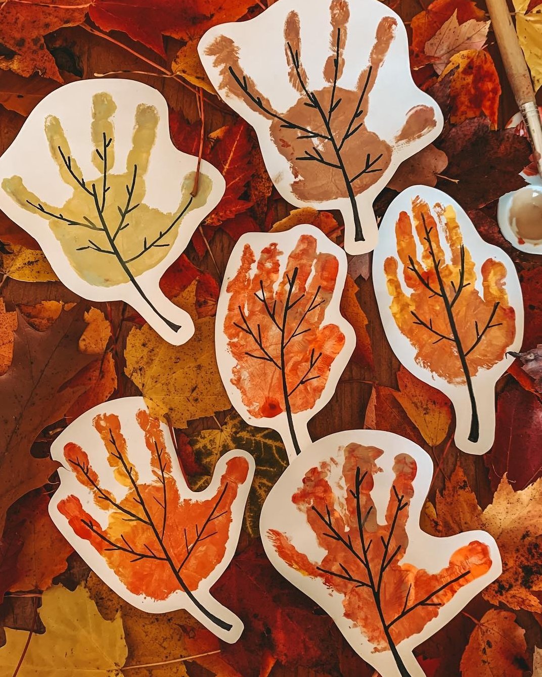 Handprint fall leaf crafts for kids in orange, yellow, and brown with black branch details