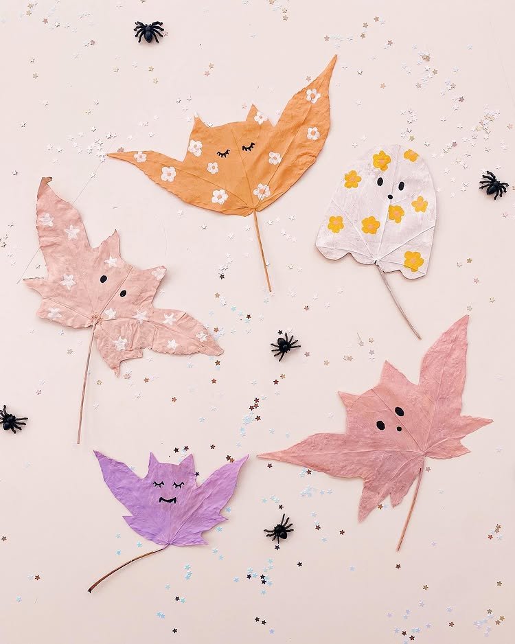 Painted autumn leaves styled as friendly bats and ghosts with flowers, spiders, and sparkly confetti