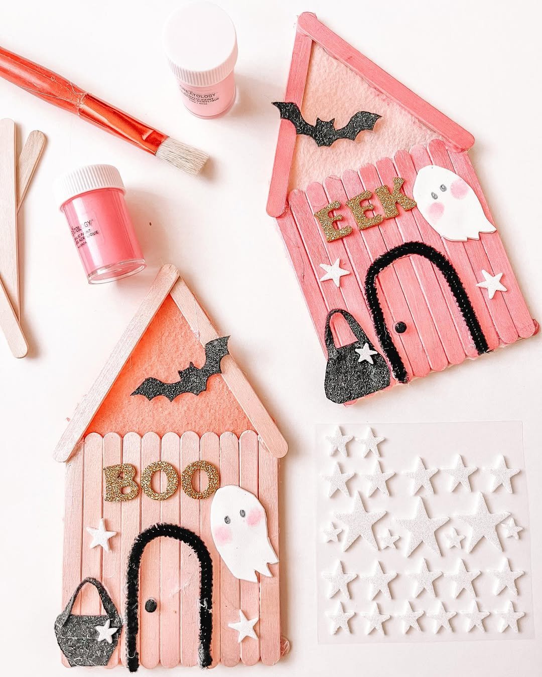 Pink popsicle stick haunted houses with ghosts, bats, glitter letters, and stars for spooky kids' crafts