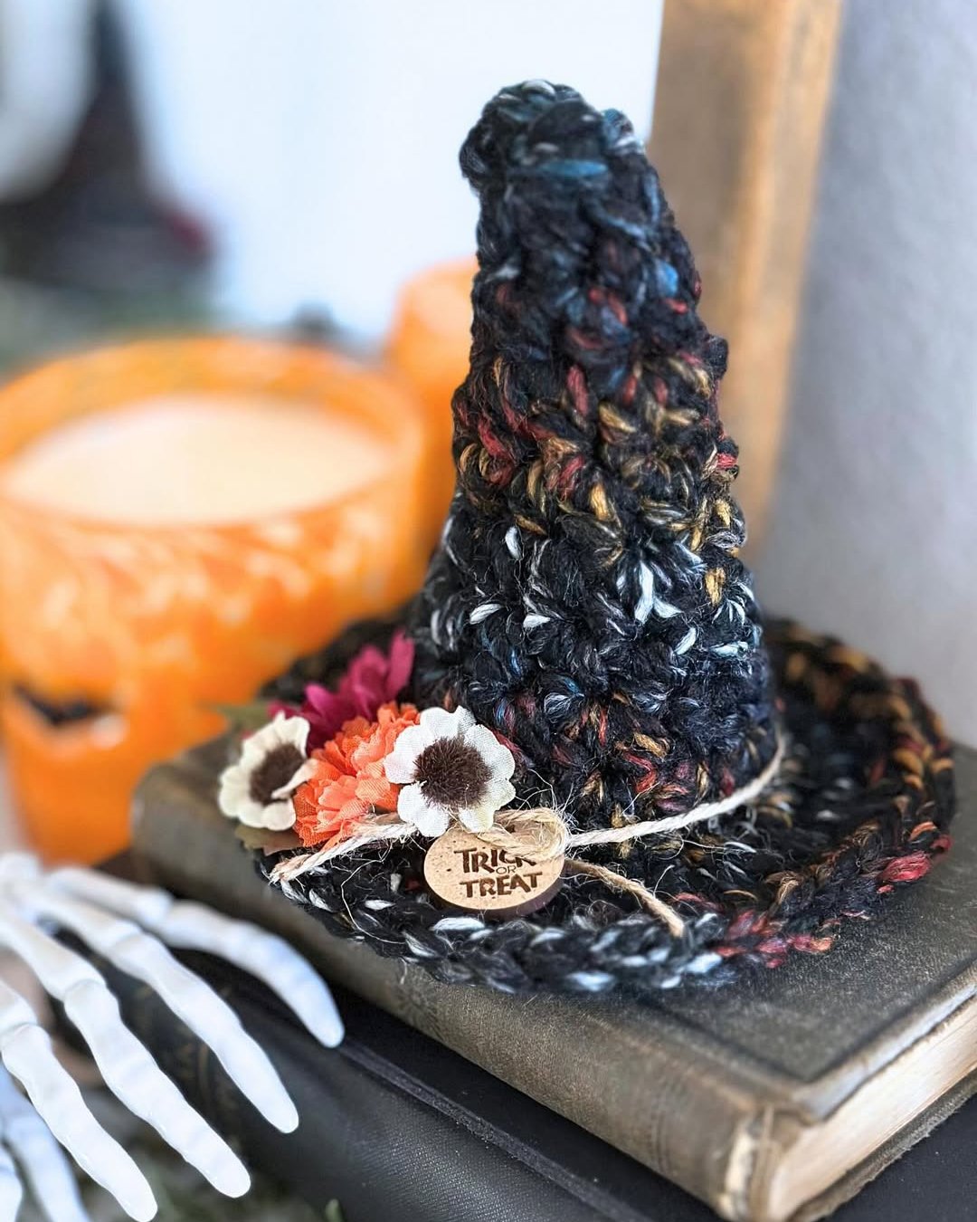 Crocheted black witch hat with flowers, pumpkin decor, wooden trick-or-treat tag, and spooky autumn styling