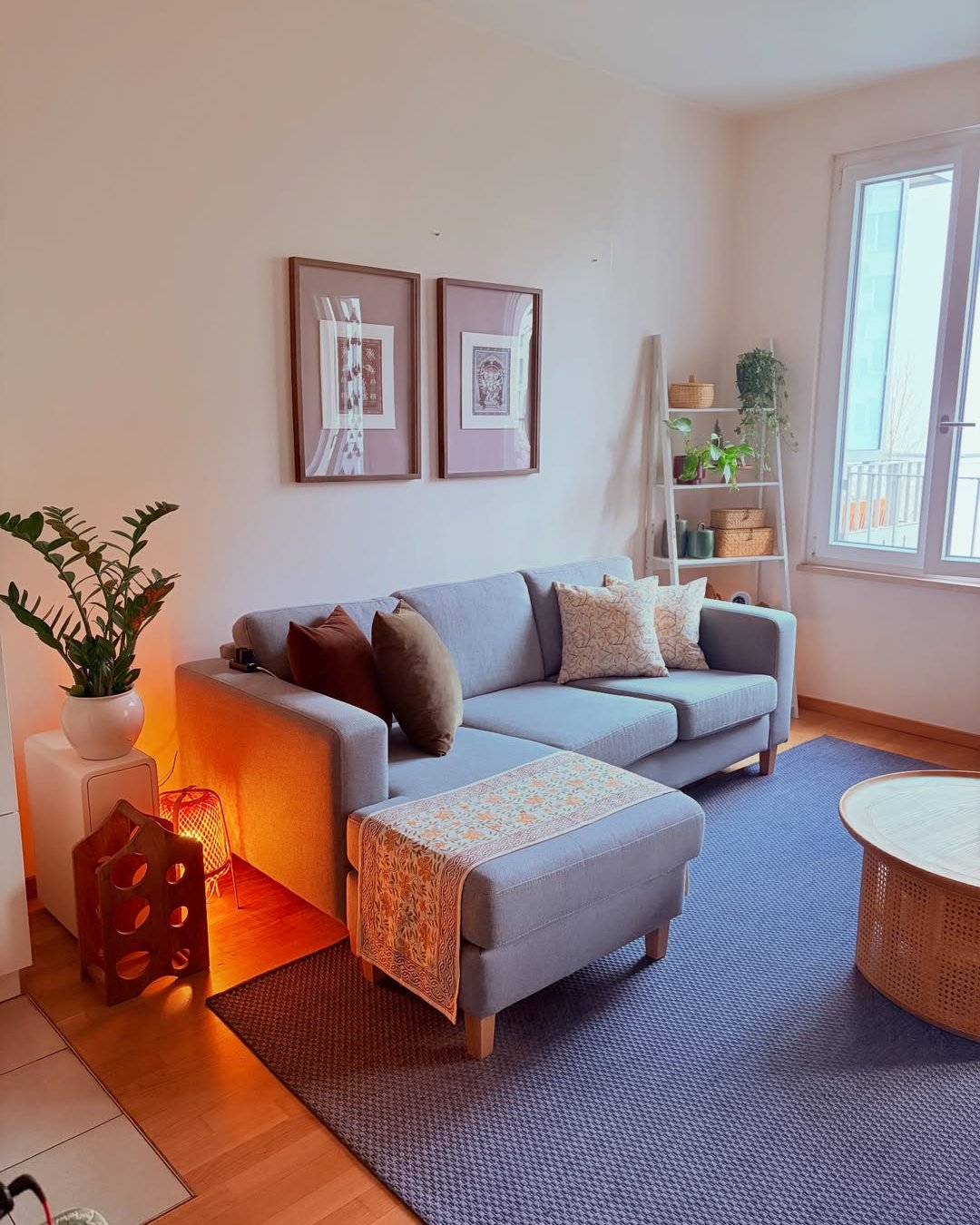 Cozy winter lounge with gray sofa, amber lamp, woven rug, botanical accents, and soft neutral artwork