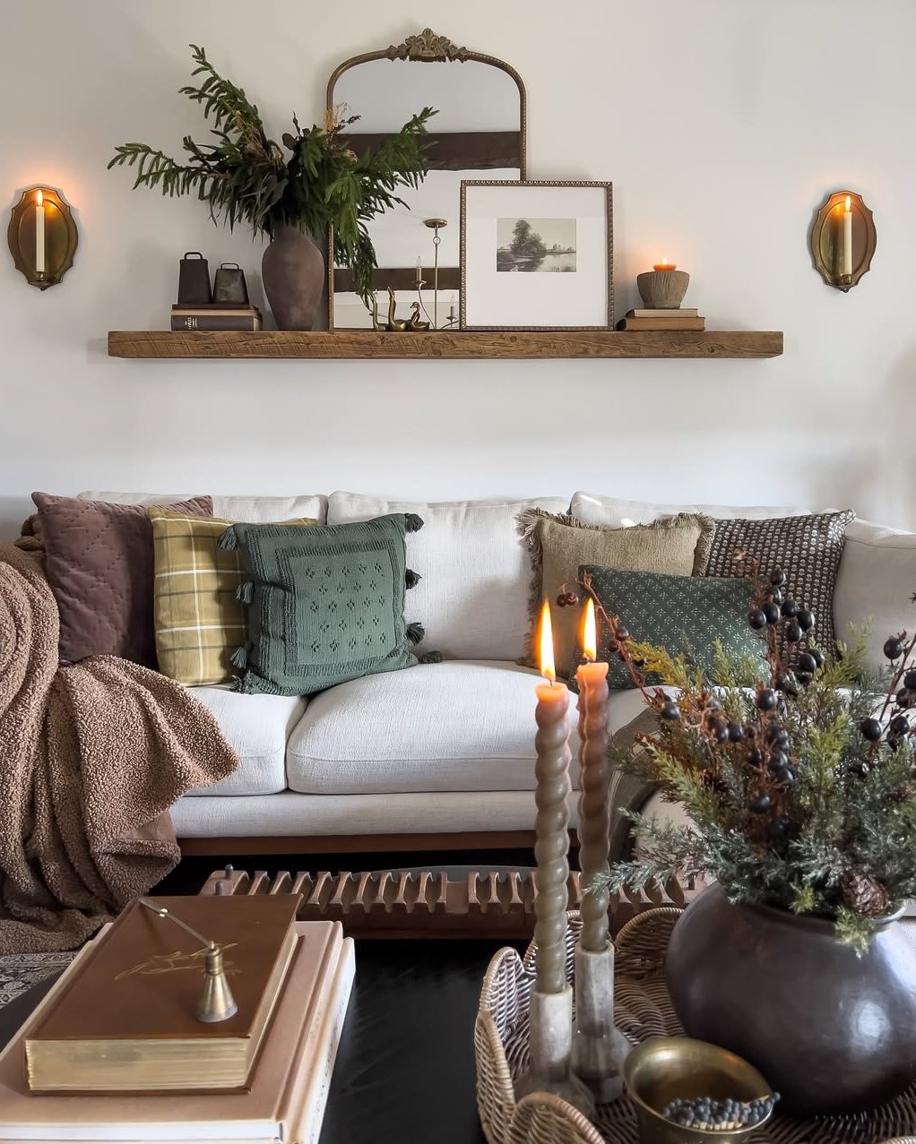 Winter living room decor ideas with a rustic shelf, greenery, candles, cushions, and cozy neutral furnishings