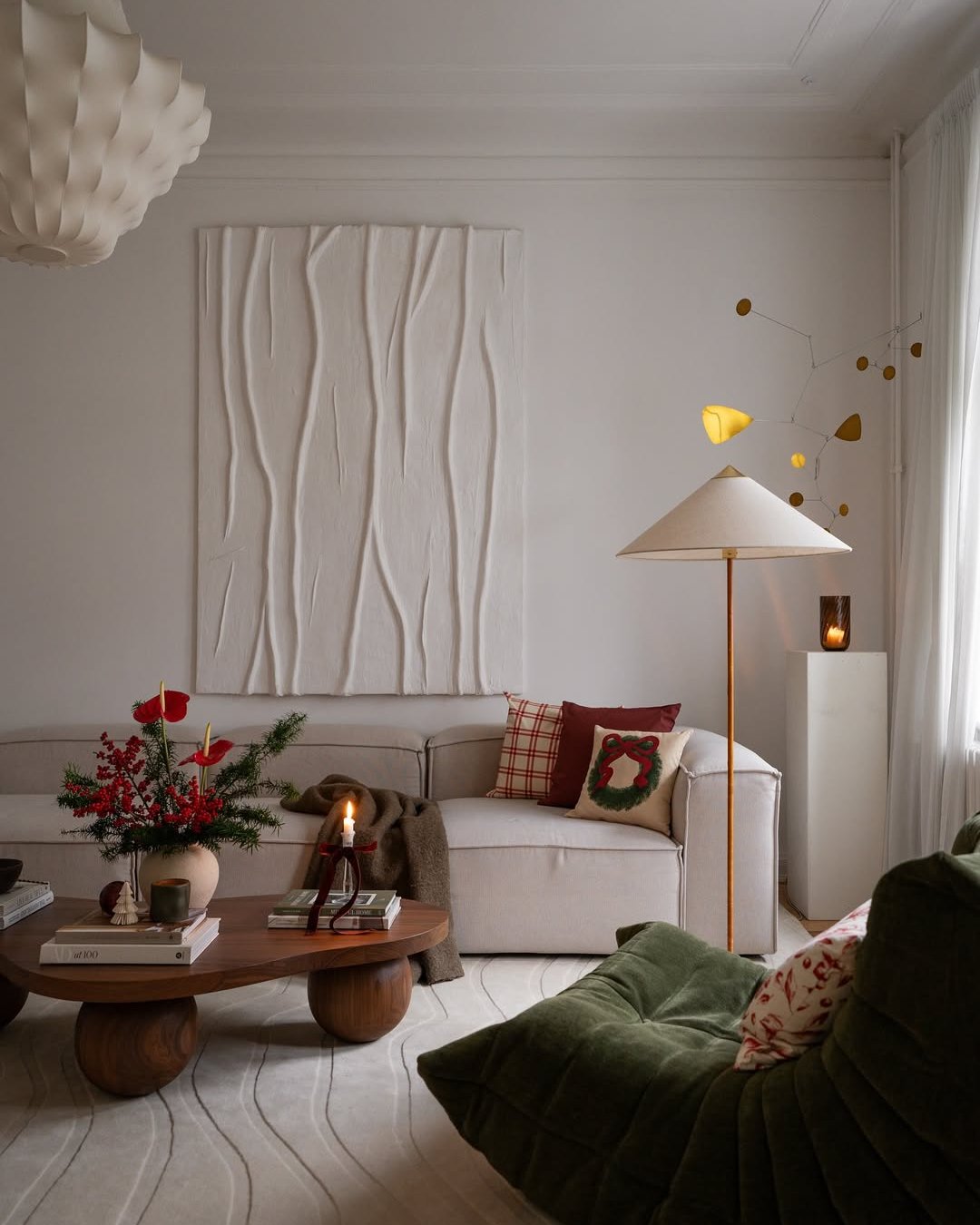 Soft neutral winter living room with textured wall art, greenery, candlelight, and festive pillows