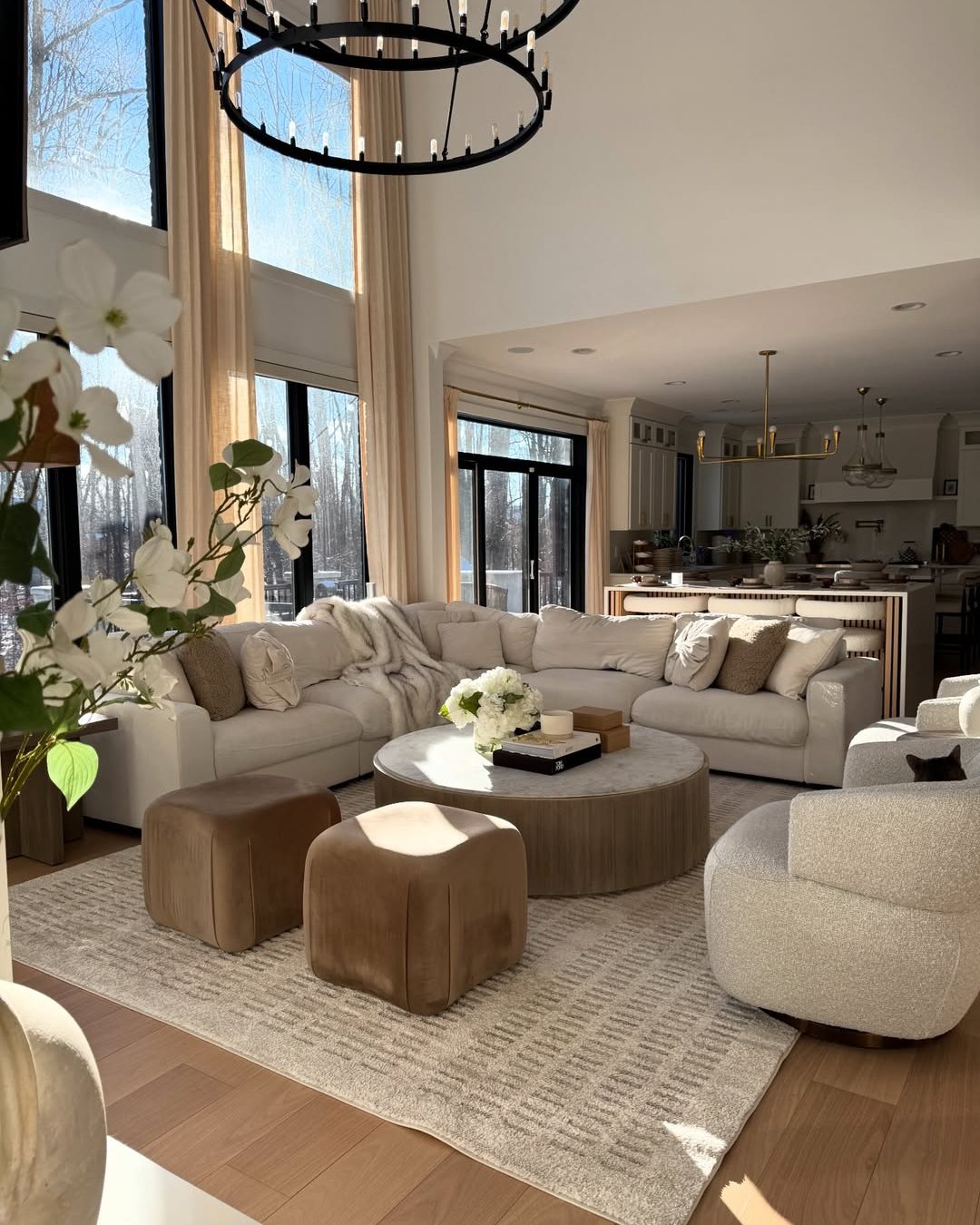 Layered neutral living room with boucle seating, velvet ottomans, soft textiles, and a statement ring chandelier