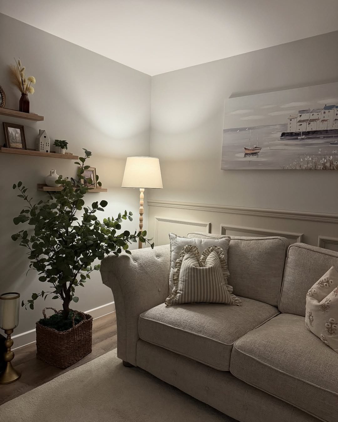 Warm neutral lounge with layered pillows, soft lamplight, leafy greenery, and woven winter accents